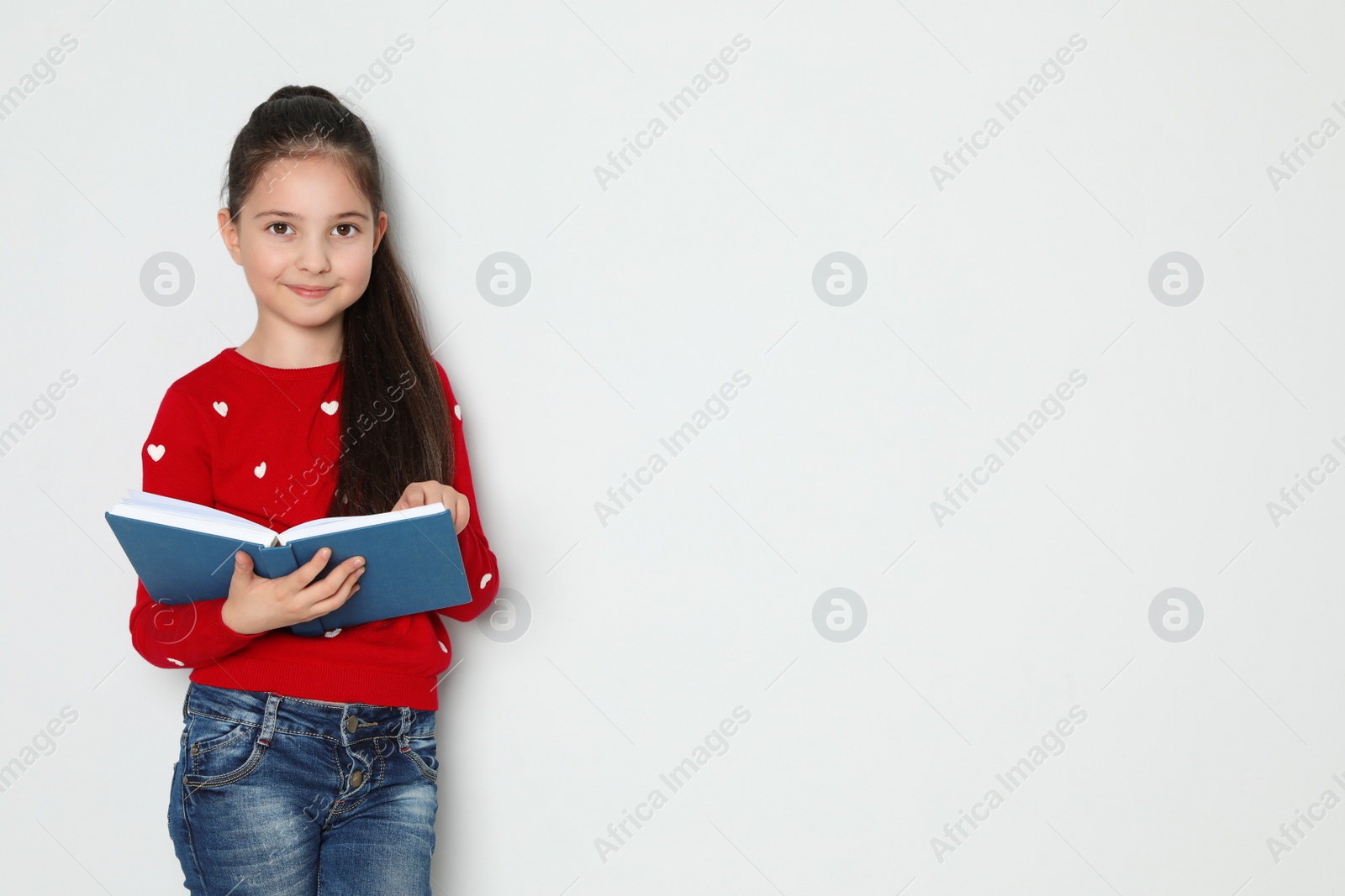 Photo of Cute little girl reading book on white background, space for text