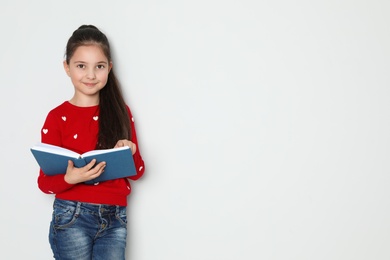 Photo of Cute little girl reading book on white background, space for text