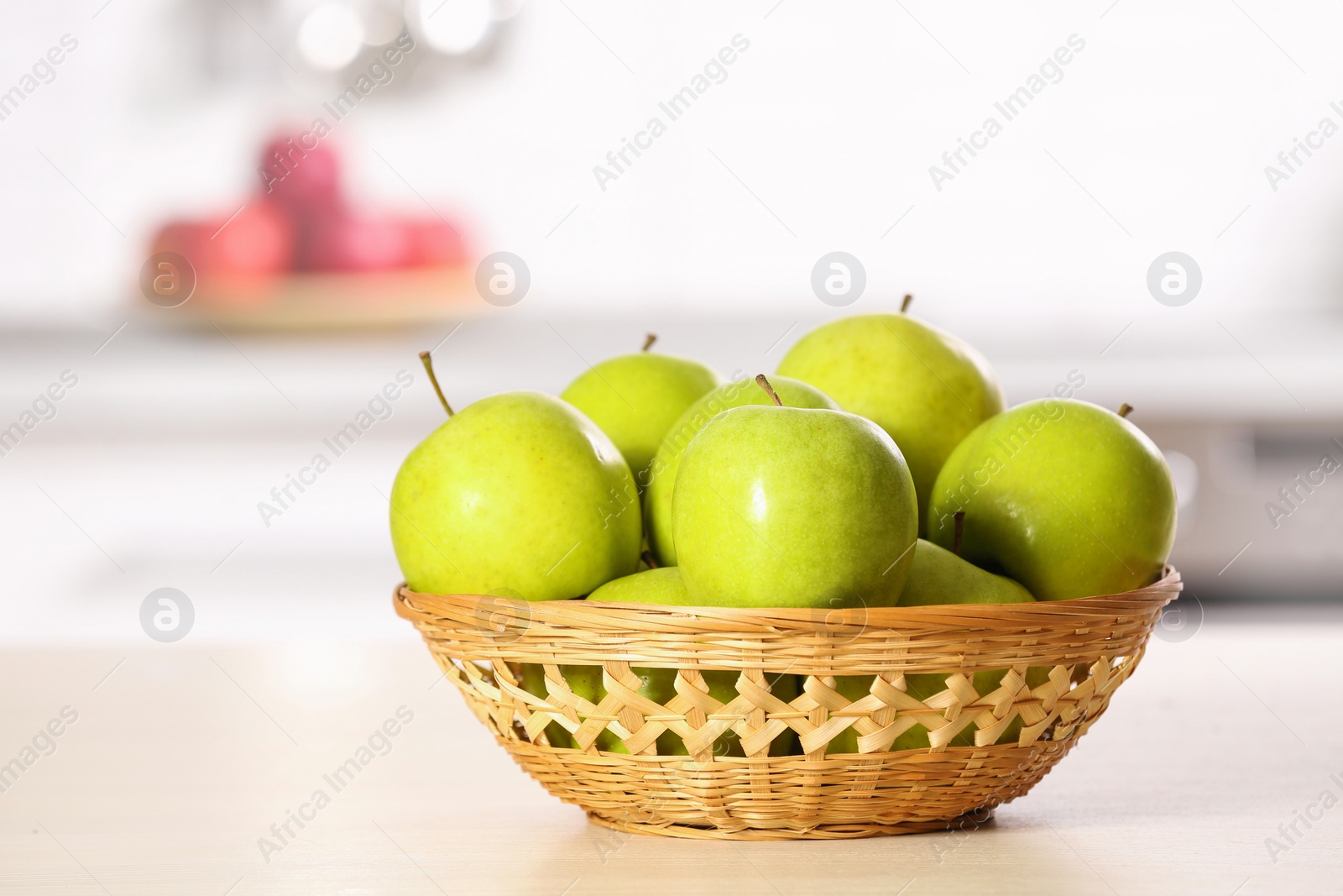 Photo of Wicker bowl with sweet green apples on table in kitchen