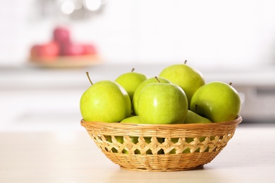 Photo of Wicker bowl with sweet green apples on table in kitchen