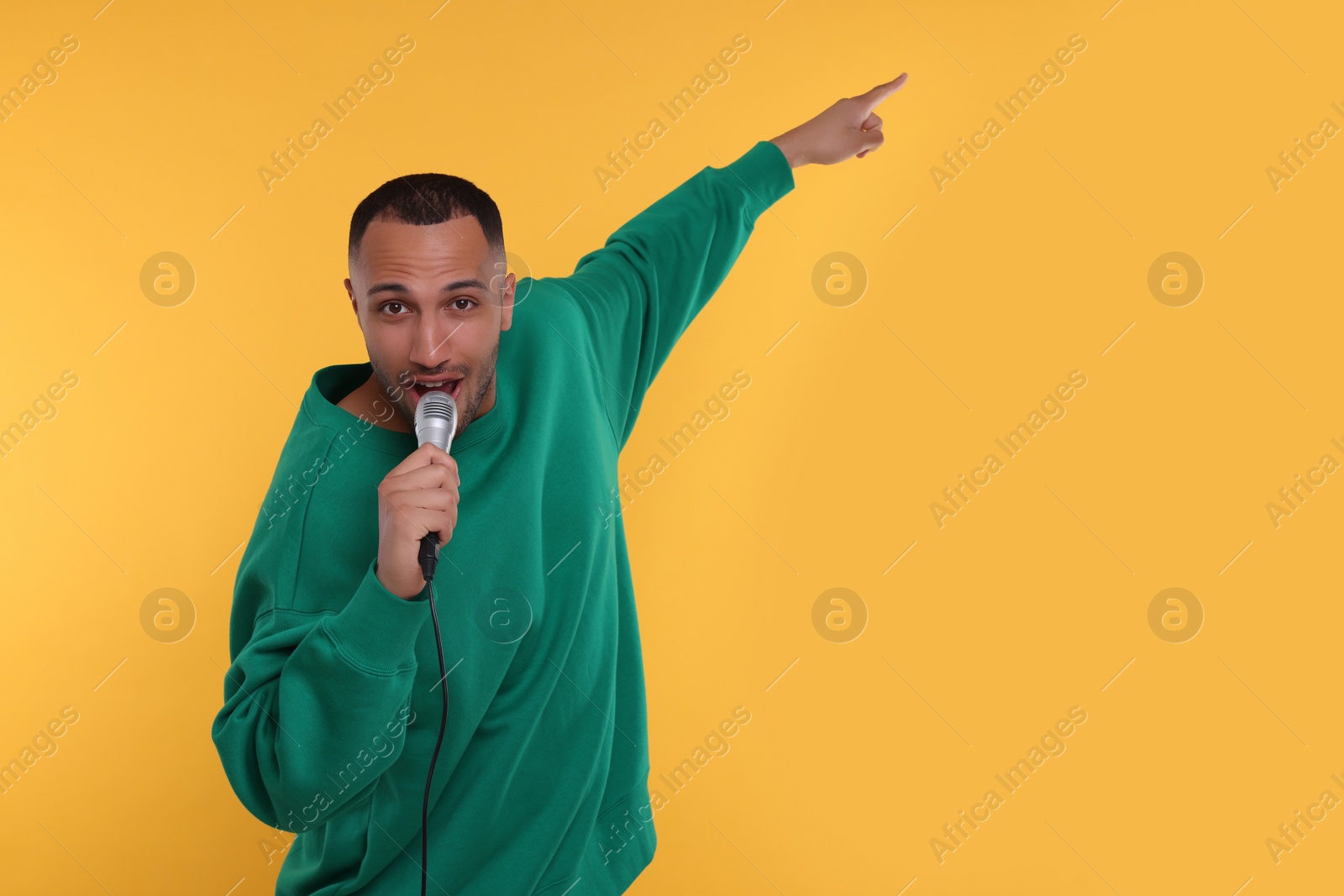 Photo of Handsome man with microphone singing on orange background. Space for text