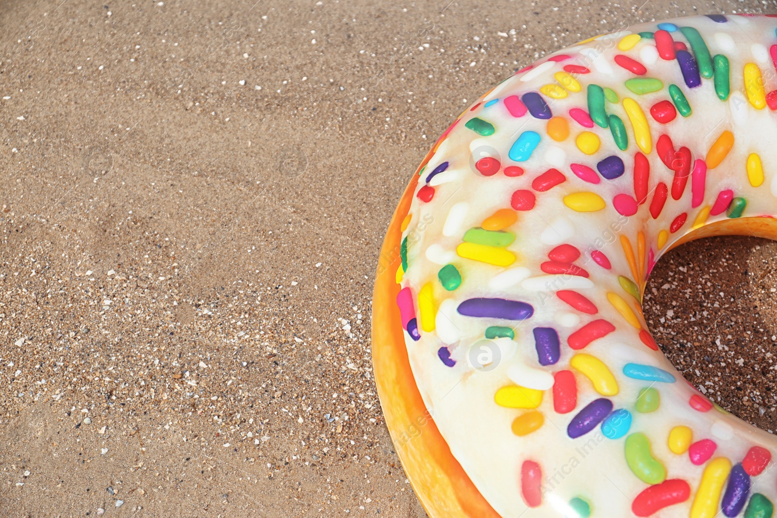 Photo of Bright inflatable doughnut ring on sandy beach. Space for text