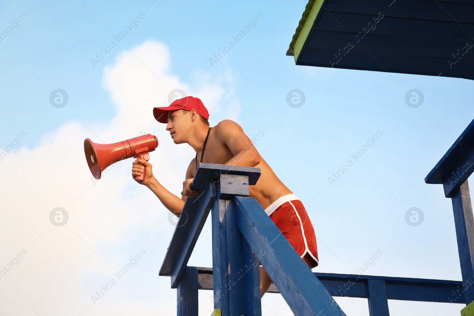 Photo of Handsome lifeguard with megaphone on watch tower against sky