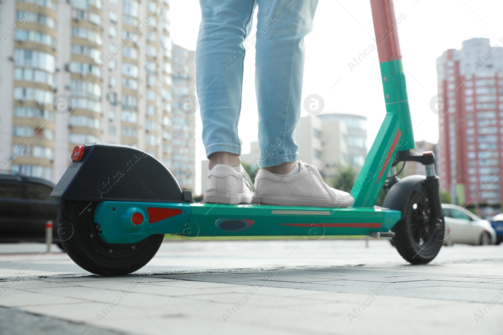 Photo of Man riding modern electric kick scooter on city street, closeup