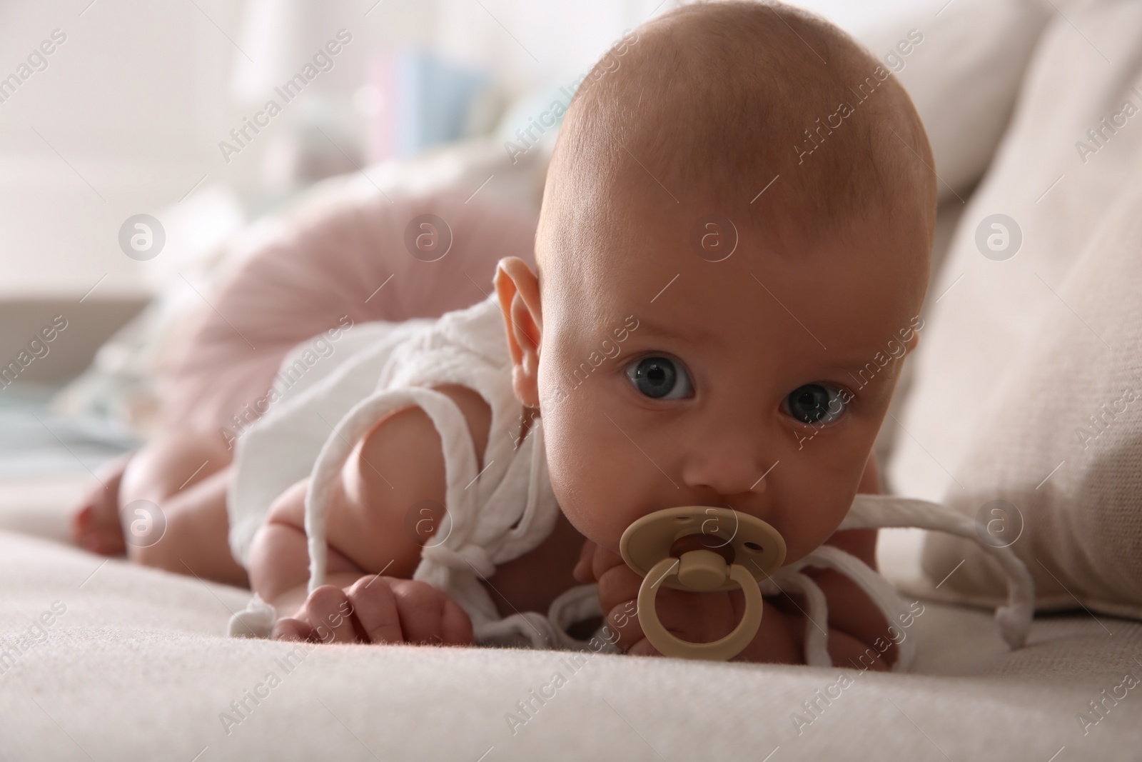 Photo of Cute little baby with pacifier on sofa at home