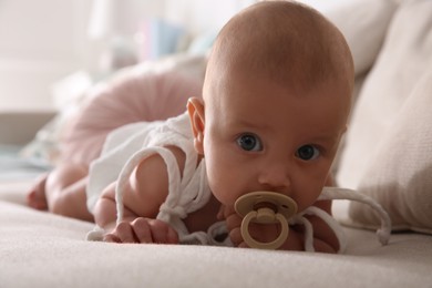 Cute little baby with pacifier on sofa at home