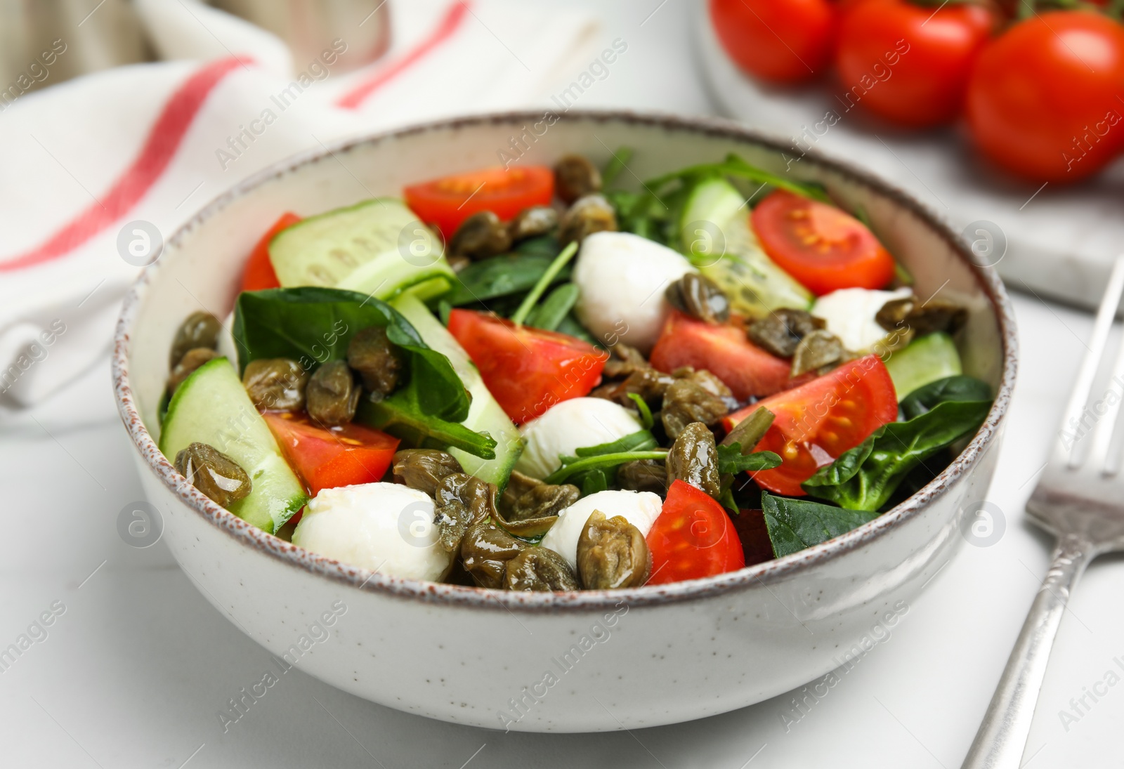 Photo of Salad with vegetables, capers and mozzarella in bowl on table, closeup