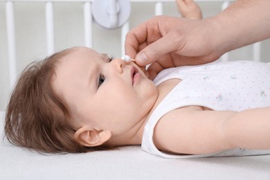 Photo of Father cleaning nose of his baby with cotton bud on bed, closeup