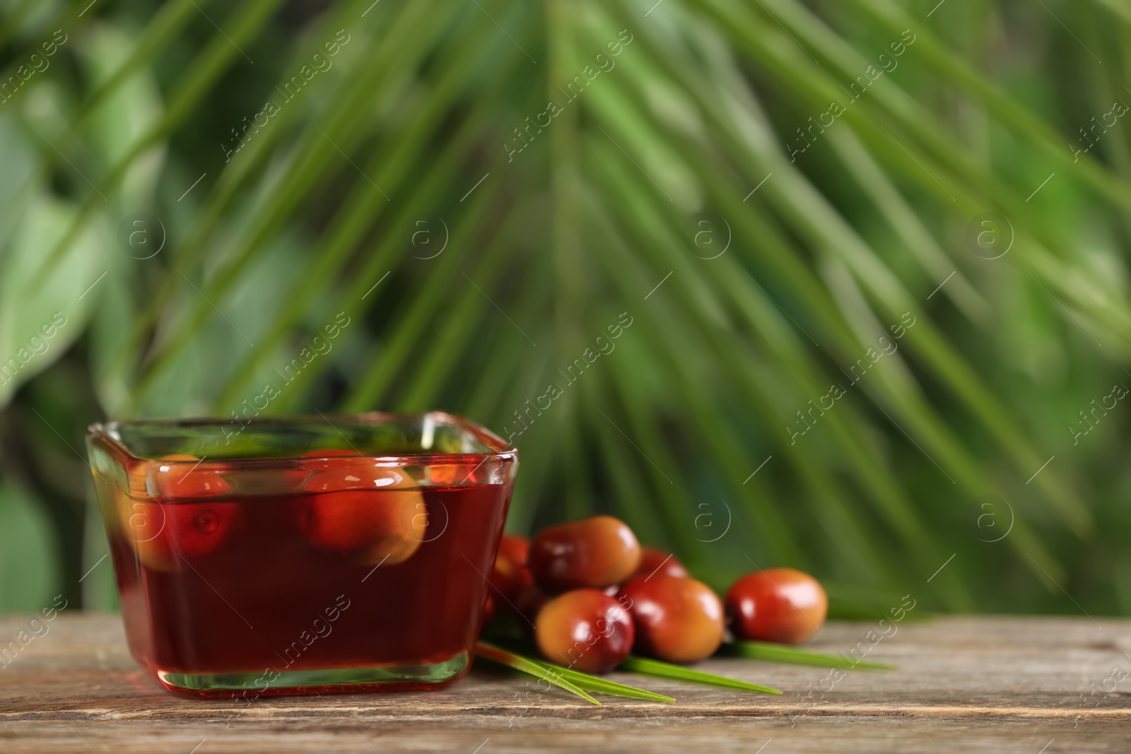 Photo of Palm oil in glass bowl, tropical leaf and fruits on wooden table. Space for text