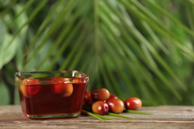 Palm oil in glass bowl, tropical leaf and fruits on wooden table. Space for text