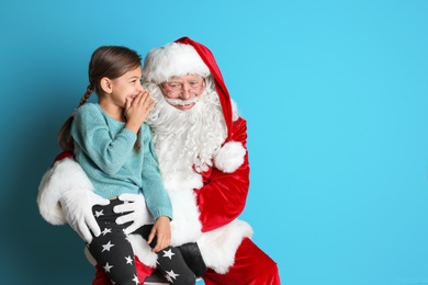 Photo of Little girl whispering in authentic Santa Claus' ear on color background