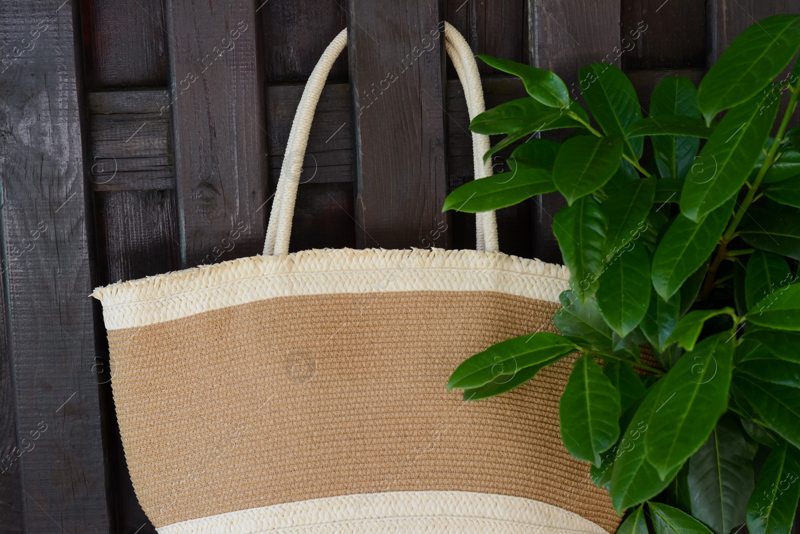 Photo of Stylish bag hanging on wooden fence outdoors. Beach accessory