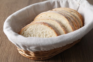 Fresh bread slices in wicker basket on wooden table, closeup