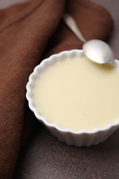 Photo of Bowl with condensed milk and spoon on brown table, closeup