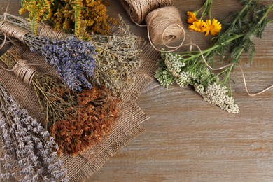 Different herbs, thread and burlap fabric on wooden table, flat lay. Space for text