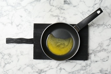 Frying pan with melting butter on marble background, top view