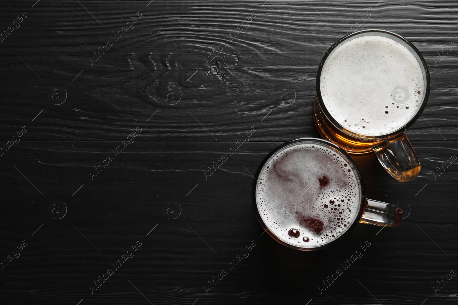 Photo of Glass mugs with different types of cold tasty beer on wooden background, top view