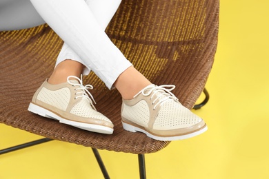 Woman in stylish shoes sitting on chair, color background