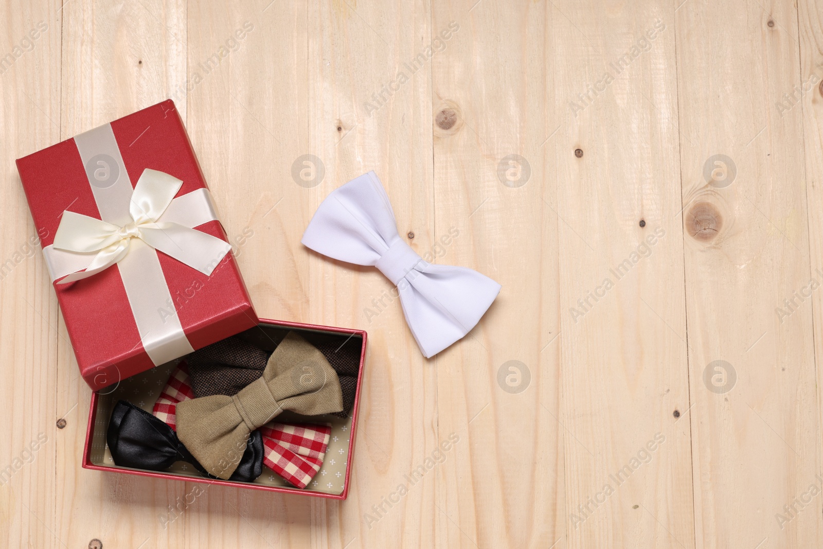 Photo of Stylish color bow ties in gift box on wooden background, flat lay. Space for text