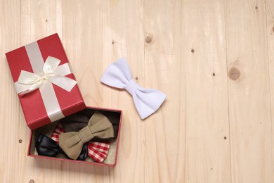 Stylish color bow ties in gift box on wooden background, flat lay. Space for text