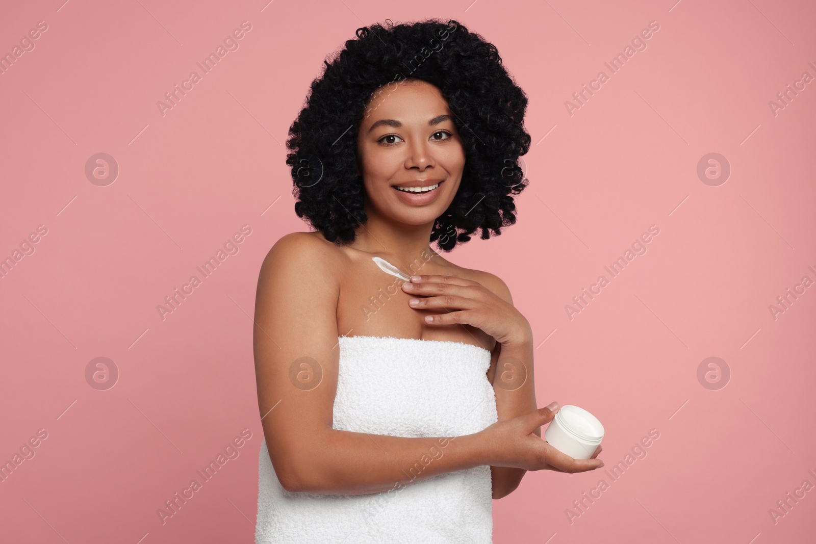 Photo of Young woman applying cream onto body on pink background