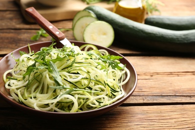 Photo of Tasty zucchini pasta with arugula on wooden table. Space for text