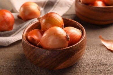 Photo of Bowl with many ripe onions on wooden table