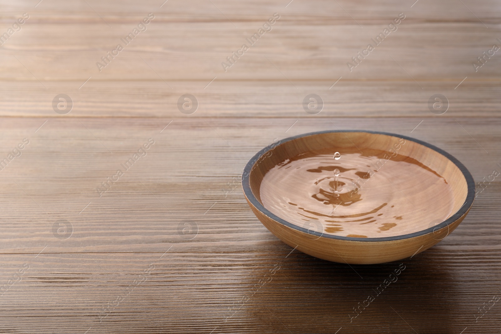 Photo of Drop falling down into bowl with clear water on wooden table. Space for text
