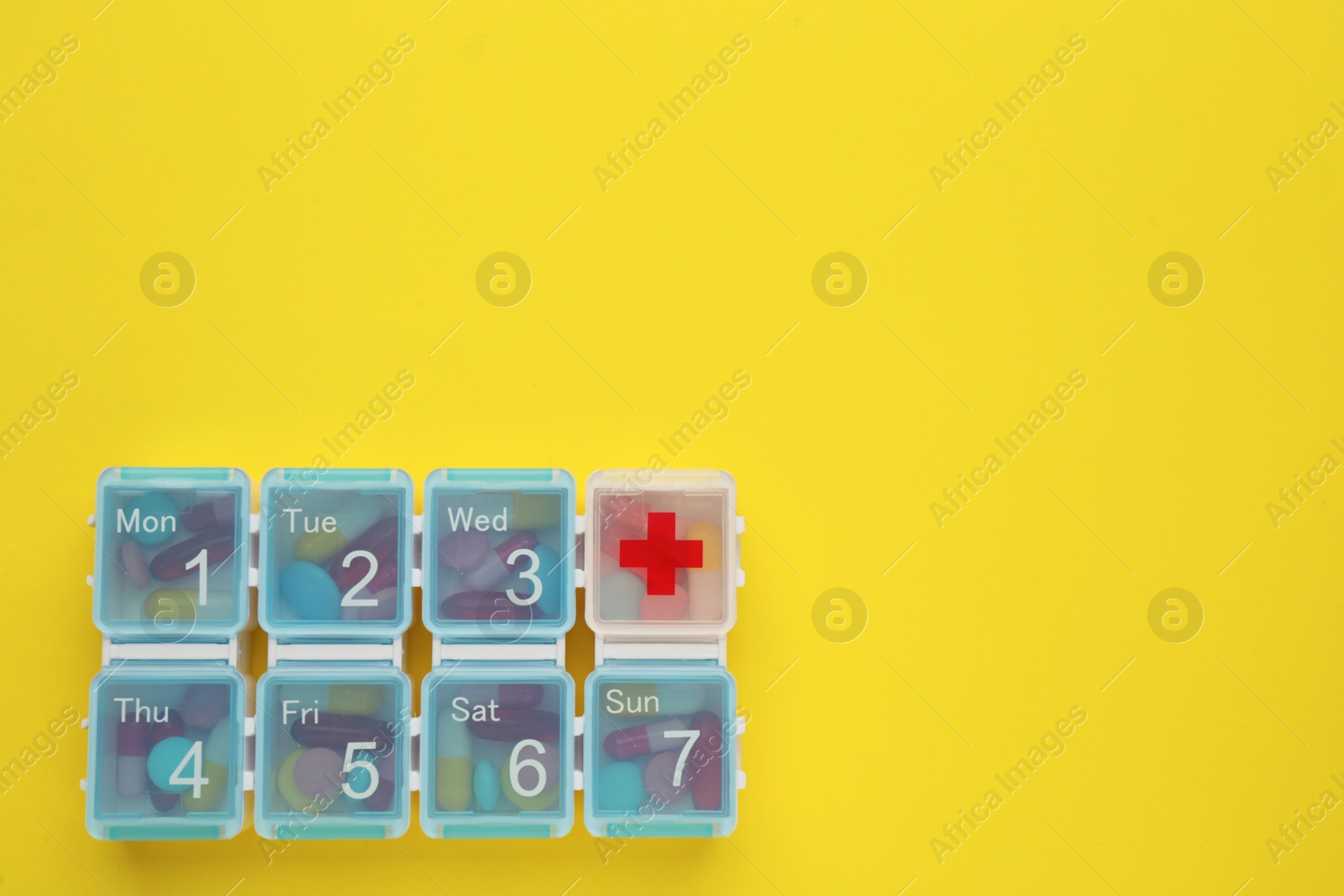 Photo of Plastic box with different pills on yellow background, top view. Space for text