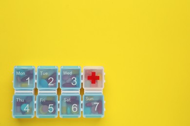 Plastic box with different pills on yellow background, top view. Space for text