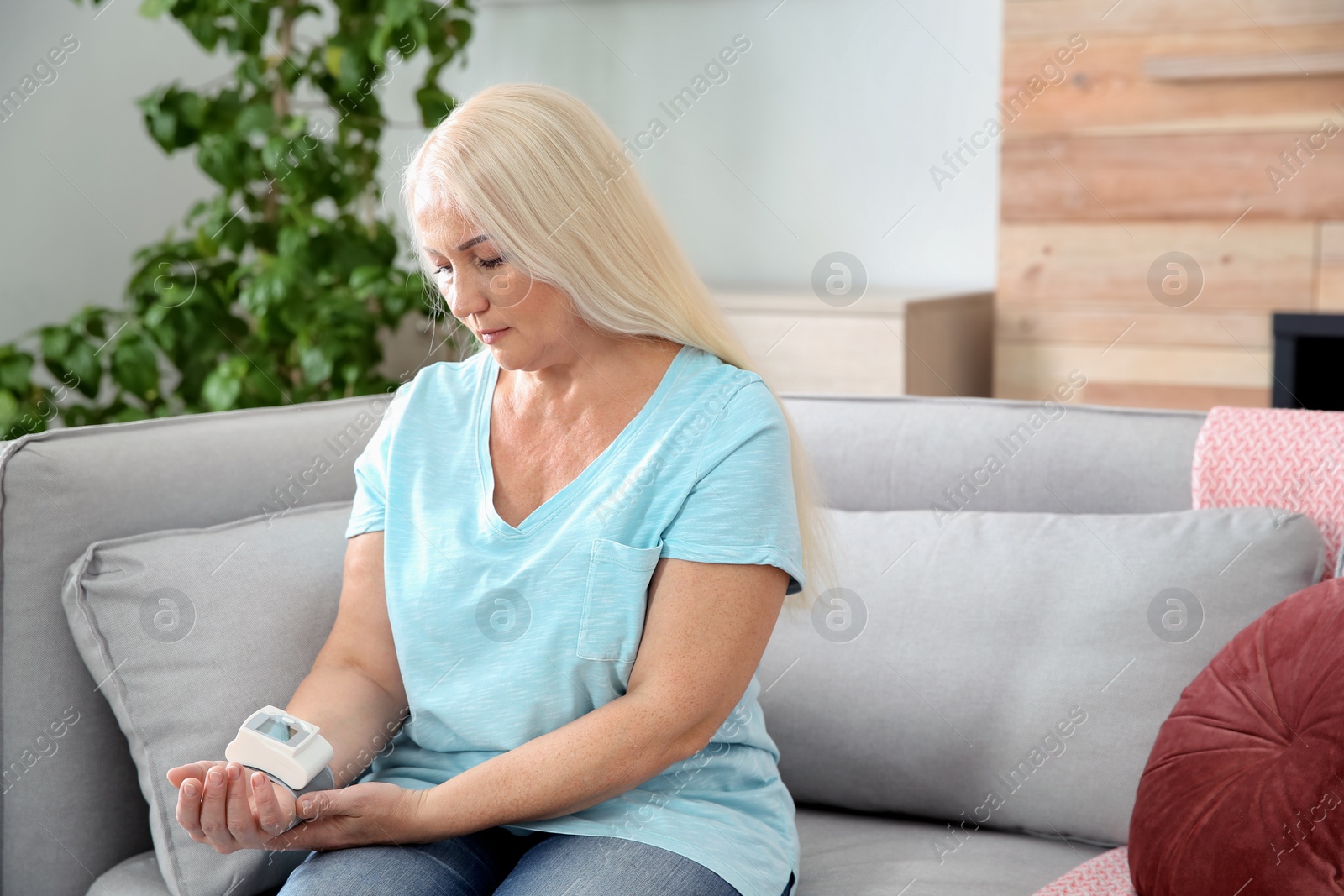 Photo of Mature woman checking pulse with medical device at home. Space for text