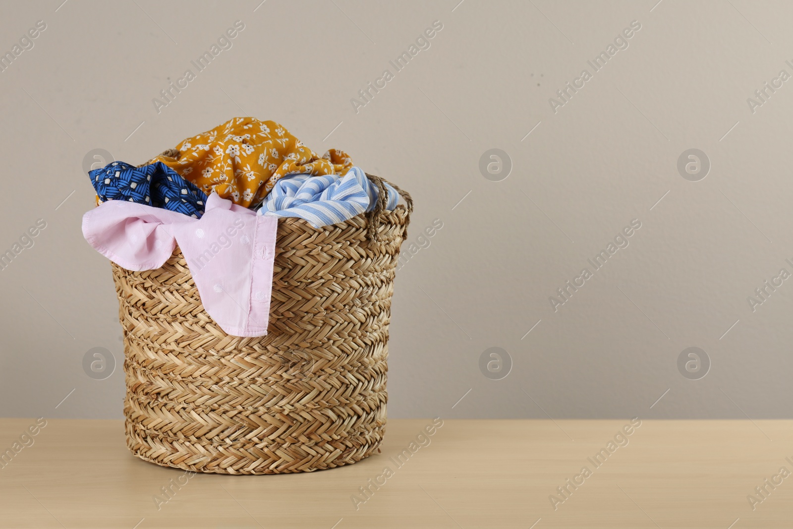 Photo of Wicker laundry basket with different clothes on wooden table. Space for text
