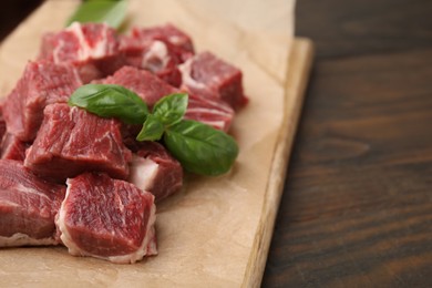 Photo of Cut fresh beef meat with basil leaves on wooden table, closeup and space for text