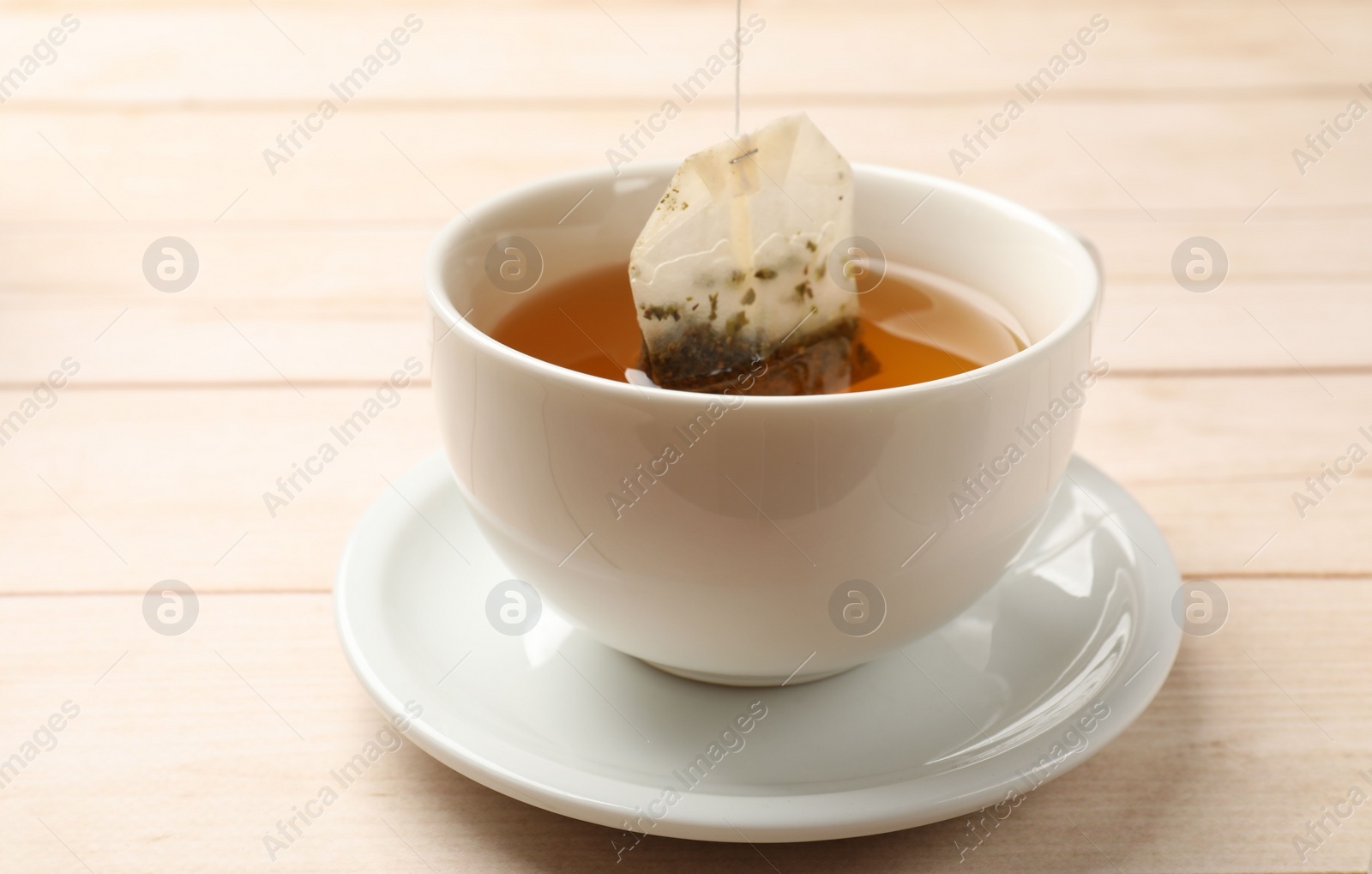 Photo of Putting tea bag in cup on light wooden table, closeup