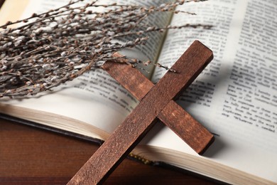 Photo of Bible, willow branches and wooden cross on table, closeup