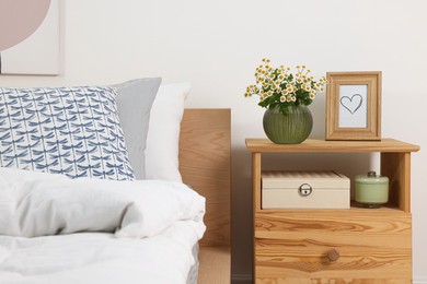 Photo of Stylish bedroom interior with bouquet of beautiful chamomile flowers on wooden nightstand