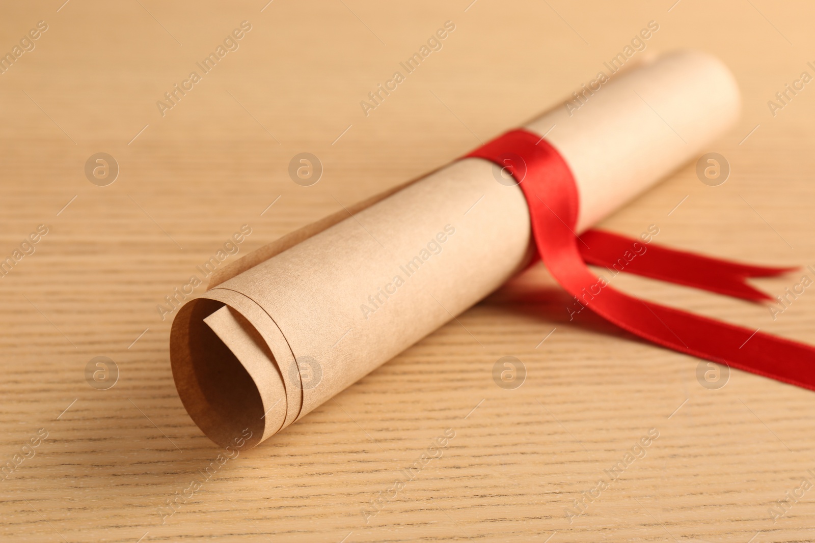 Photo of Graduation diploma tied with red ribbon on wooden table, closeup