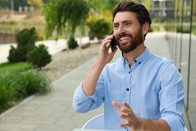 Handsome man talking on phone outdoors, space for text