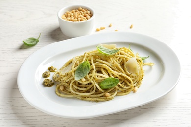 Plate with delicious basil pesto pasta on wooden table