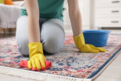 Photo of Woman in rubber gloves cleaning carpet with rag indoors, closeup