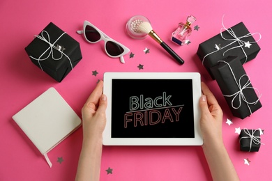 Photo of Woman with tablet surrounded by gifts and accessories on pink background, top view. Black Friday sale