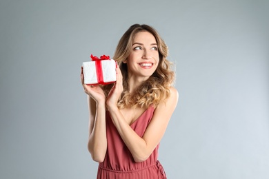 Beautiful young woman with Christmas present on light grey background