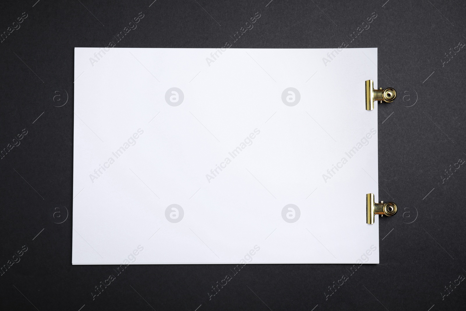 Photo of Sheet of paper with clips on black background, top view