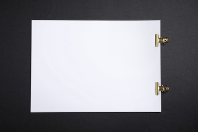 Sheet of paper with clips on black background, top view