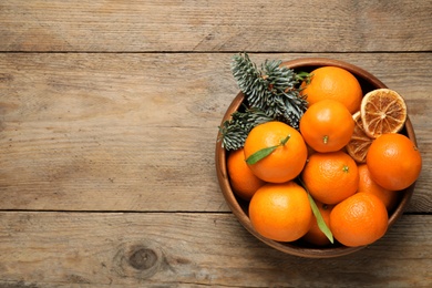 Photo of Fresh tangerines and fir tree branches in bowl on wooden table, top view with space for text. Christmas atmosphere