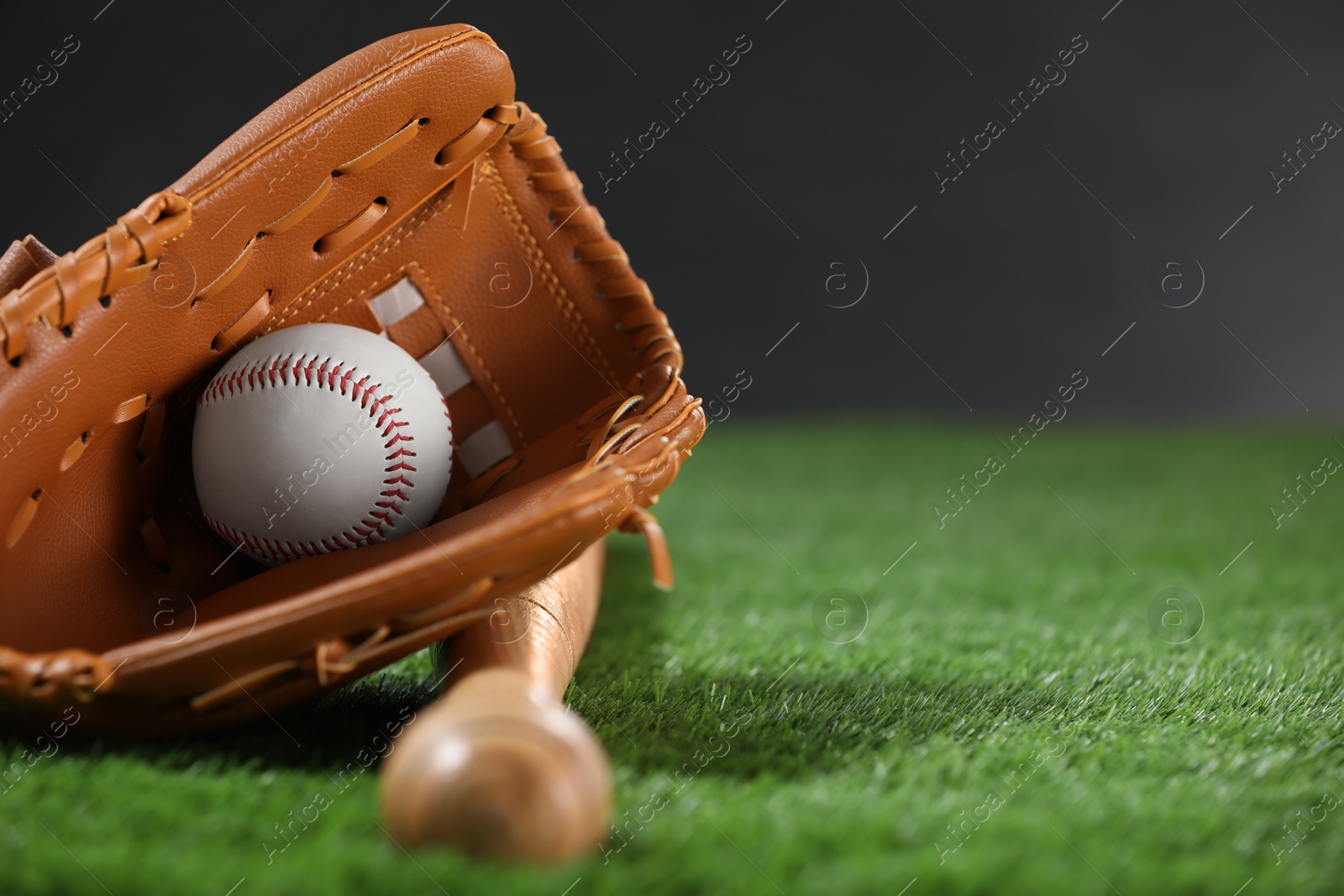 Photo of Baseball bat, leather glove and ball on green grass against dark background, closeup. Space for text
