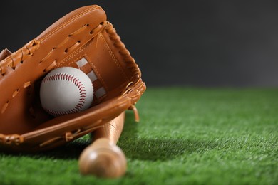 Photo of Baseball bat, leather glove and ball on green grass against dark background, closeup. Space for text