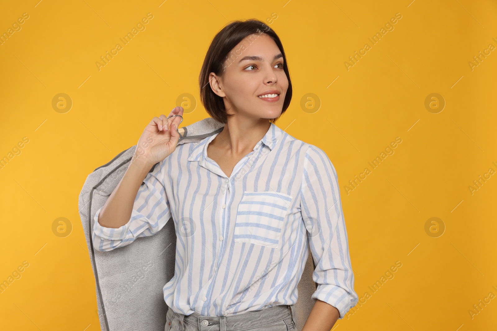 Photo of Woman holding garment cover with clothes on yellow background. Dry-cleaning service