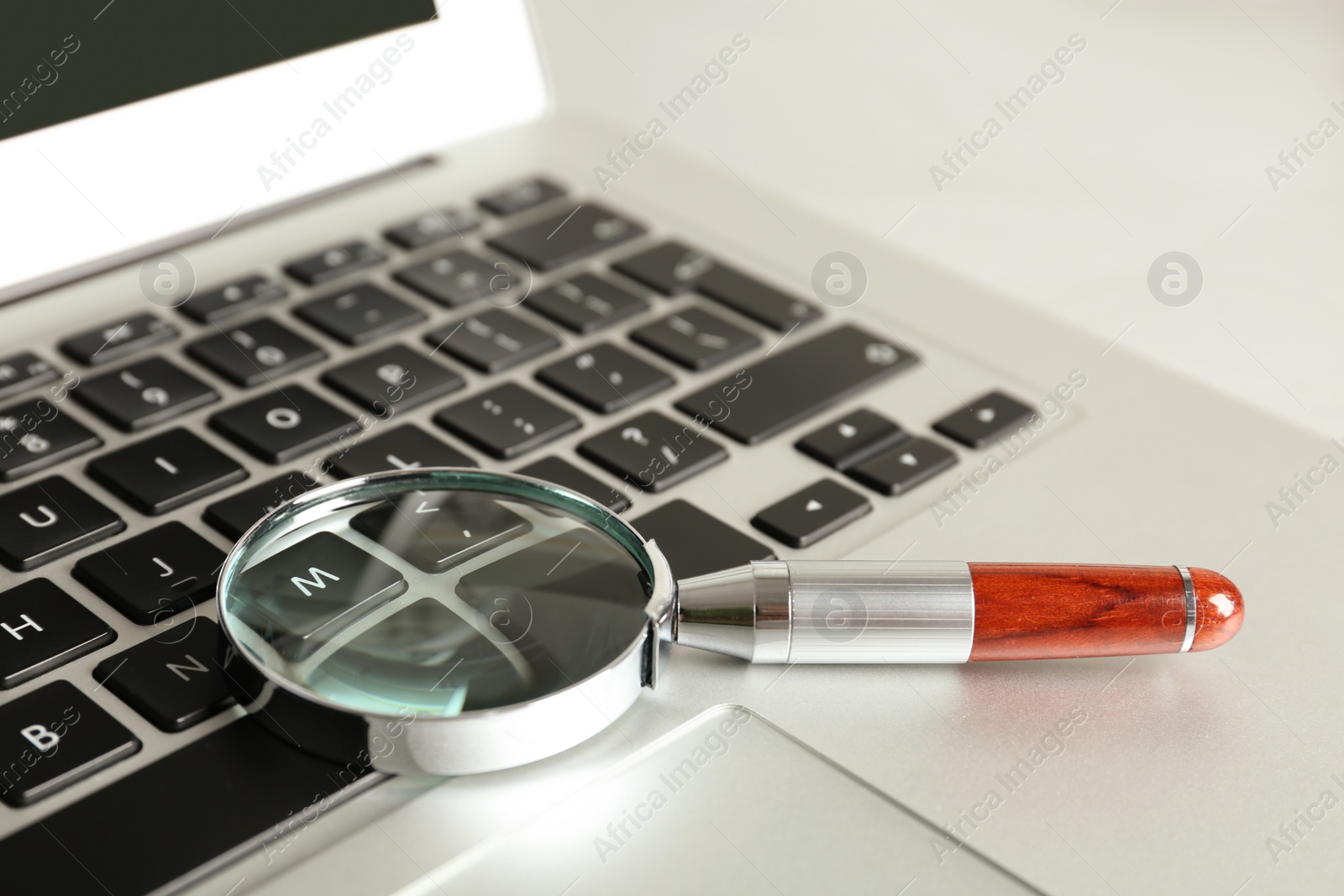 Photo of Magnifying glass and modern laptop on table, closeup. Search concept