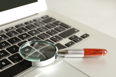 Photo of Magnifying glass and modern laptop on table, closeup. Search concept